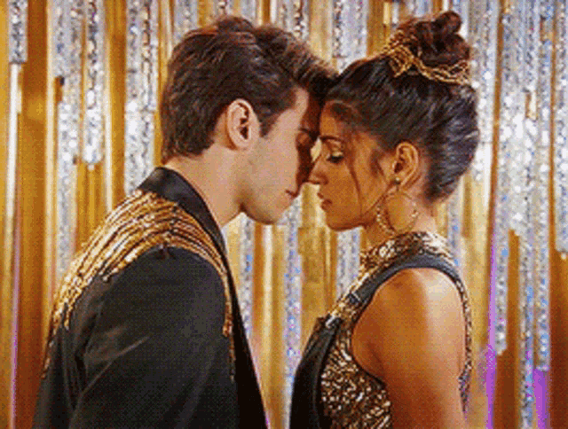 a man and woman are kissing in front of a gold curtain .
