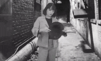 a woman in a suit is standing in an alley holding a hat