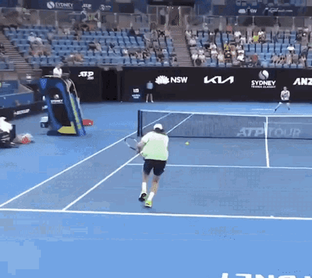 a man playing tennis on a court with a sydney advertisement on the wall behind him