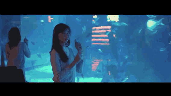 a woman stands in front of a large aquarium looking at fish