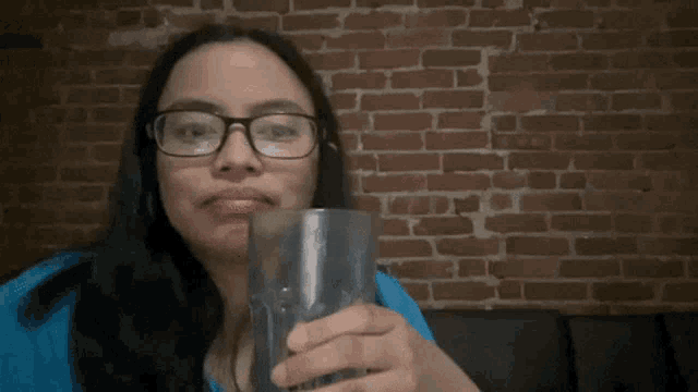 a woman with glasses holds a glass in front of a brick wall