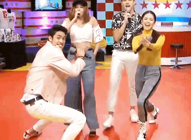 a group of people are dancing and singing into microphones on a stage .