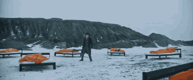 a man in a suit stands in front of a row of orange blanketed beds