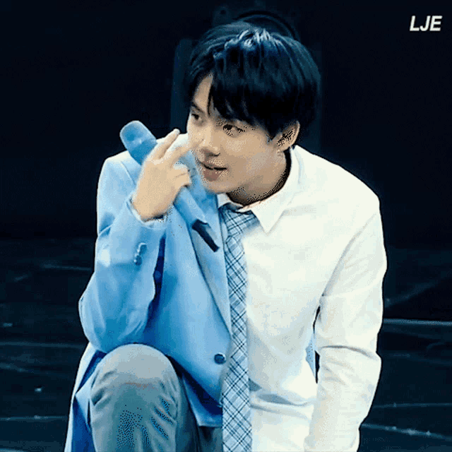 a man in a suit and tie is kneeling down and holding a microphone with the letters lje above him
