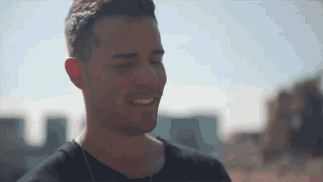 a man in a black shirt is smiling with his eyes closed in front of a city .