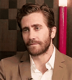 a man with a beard is wearing a suit and white shirt and making a funny face .