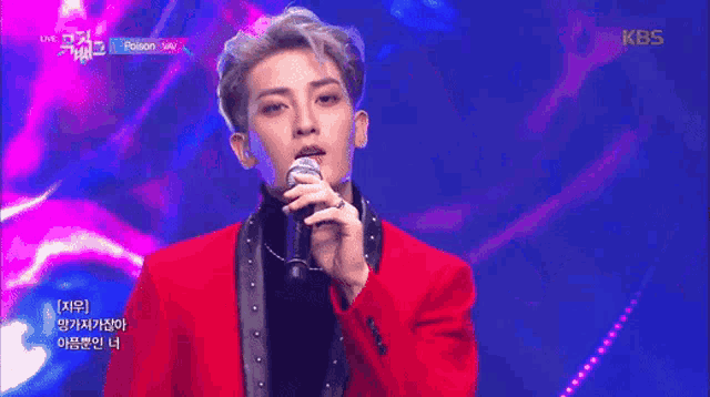 a man in a red jacket is singing into a microphone on a stage