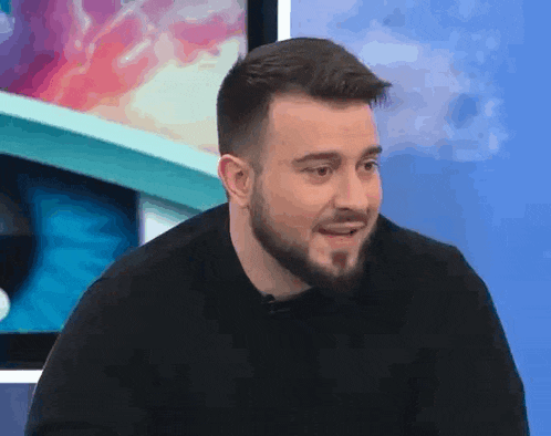 a man with a beard is making a funny face while sitting in front of a television .