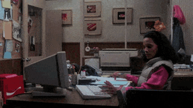 a woman sits at a desk in front of a computer and a coca cola box