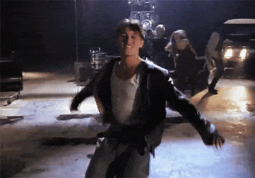 a man in a leather jacket and white tank top is dancing on a stage