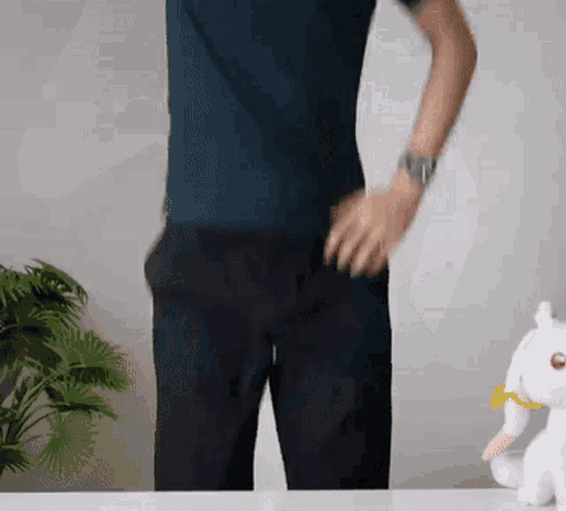 a man in a blue shirt and black pants is standing in front of a stuffed animal .