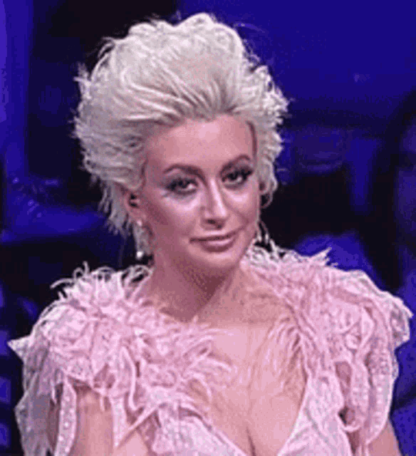 a woman in a pink dress with feathers on the sleeves is looking at the camera .