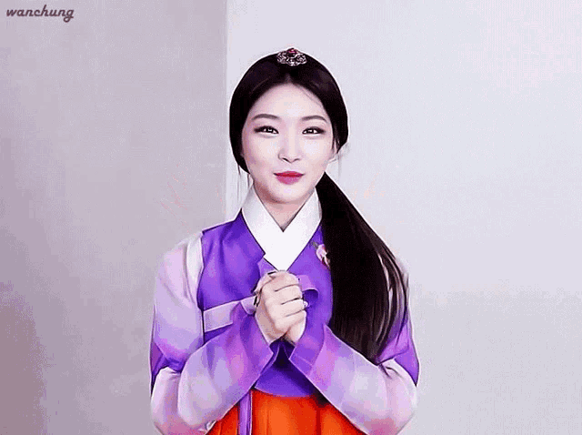 a woman wearing a purple and orange hanbok with her hands folded in front of her face .
