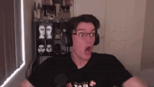 a man wearing headphones and glasses is making a surprised face while sitting in front of a window .