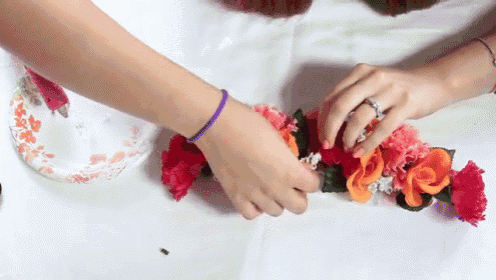a woman wearing a purple bracelet and a wedding ring is arranging flowers on a table .
