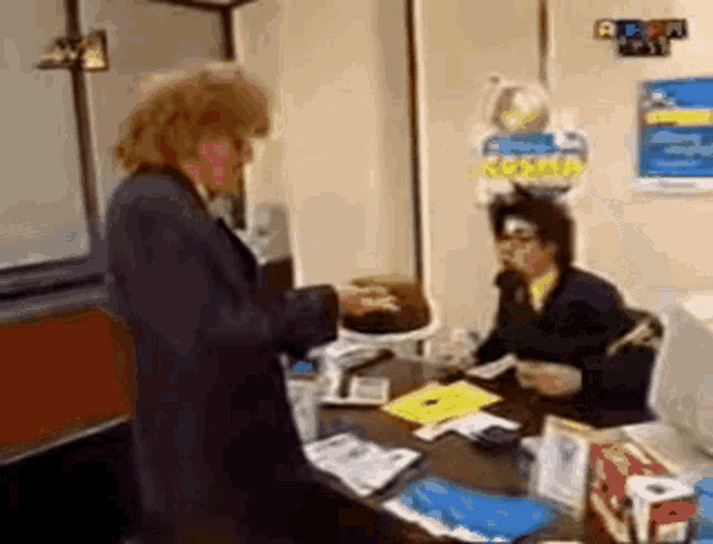 a man in a suit is standing in front of a desk with a woman sitting at it .