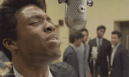 a man is singing into a microphone with a group of men standing behind him .