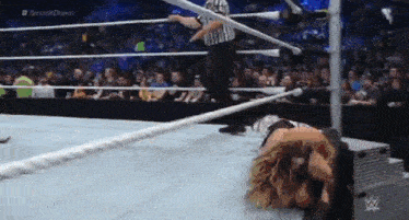a wrestler is laying on the ground in a wrestling ring with a referee in the background .