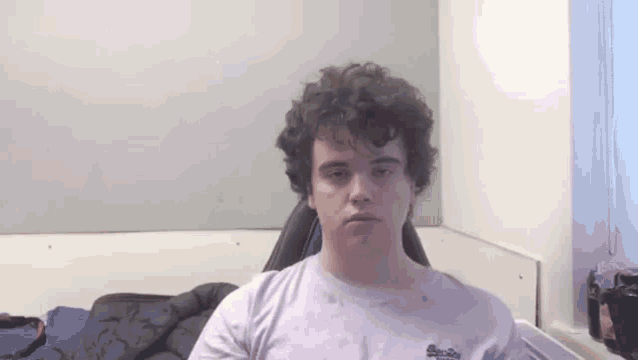 a young man with curly hair is sitting in a chair in a room .