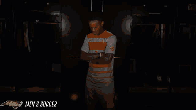 a man stands in a dark locker room with the words men 's soccer behind him