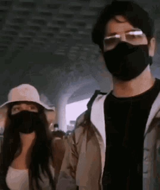 a man and a woman wearing masks and glasses are standing next to each other at an airport .