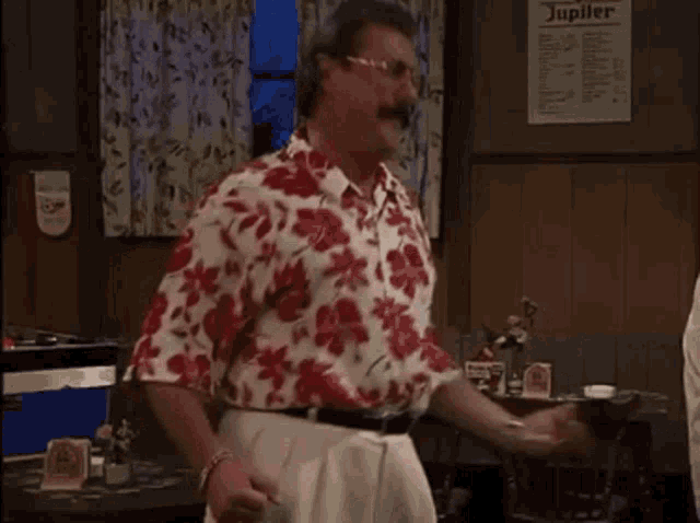 a man in a red and white floral shirt is dancing in a room with a sign that says jupiter on it .