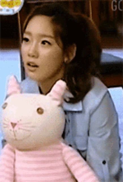 a woman is holding a stuffed cat with a pink tail