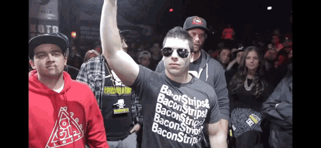 a man wearing a shirt that says bacon strips holds up his hand