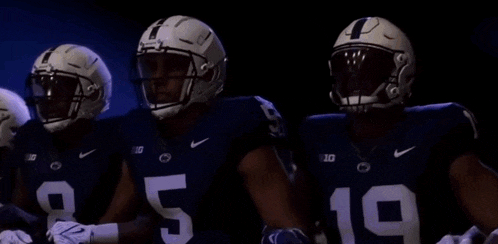 three football players are standing next to each other in a dark room .