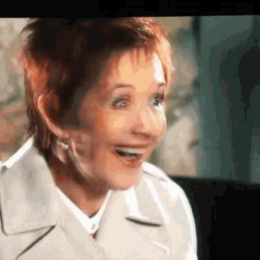 a woman with red hair is smiling and wearing a white jacket .