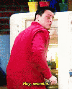 a man in a red shirt is standing in front of a refrigerator and saying hey sweetie