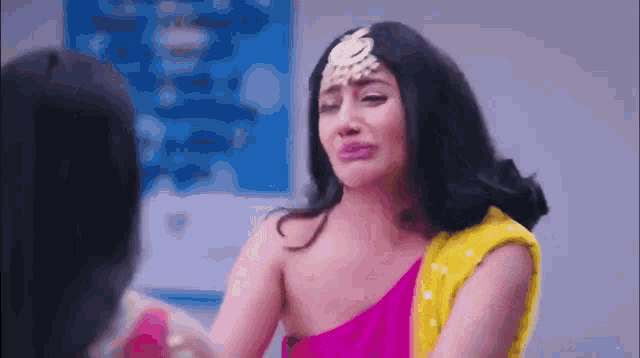 a woman in a pink one shoulder top and a yellow sari is crying .