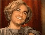 a man with long hair is smiling and wearing a wig .