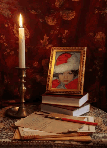 a framed picture of a girl wearing a santa hat sits on top of a stack of books next to a lit candle