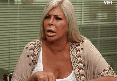 a woman with a tattoo on her arm is sitting in front of a window with blinds and making a funny face .