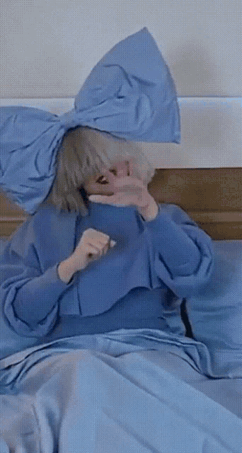 a woman in a blue dress is laying on a bed covering her face with her hand