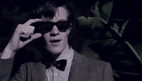 a man wearing sunglasses and a bow tie looks at the camera