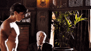 a shirtless man stands next to an older man in a suit