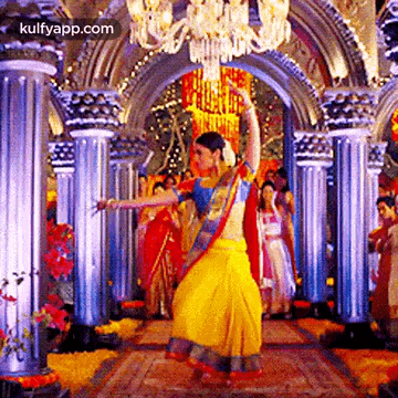 a woman in a yellow skirt is dancing in a room with columns and a chandelier .