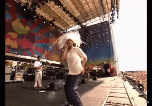 a man in a white hat sings into a microphone on a stage in front of a crowd