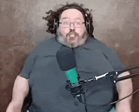 a man with a beard and glasses is standing in front of a microphone .