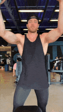 a man wearing a black tank top and a baseball cap is lifting weights in a gym