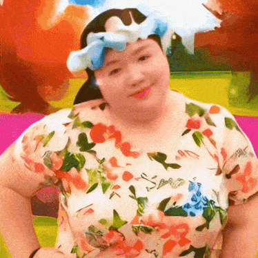 a woman wearing a floral shirt and a blue bow on her head is smiling