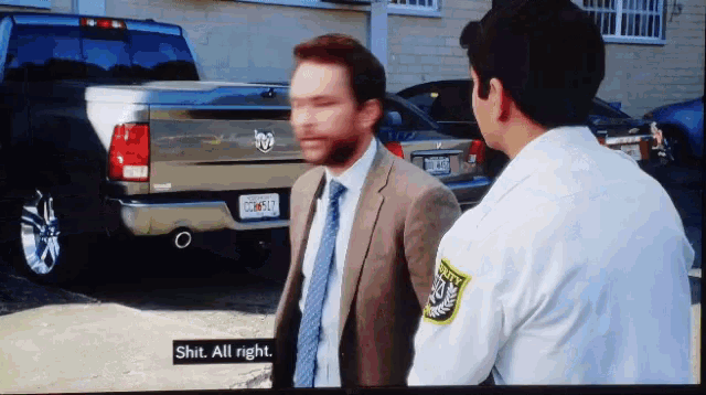 a man in a suit and tie is talking to a police officer in front of a dodge truck