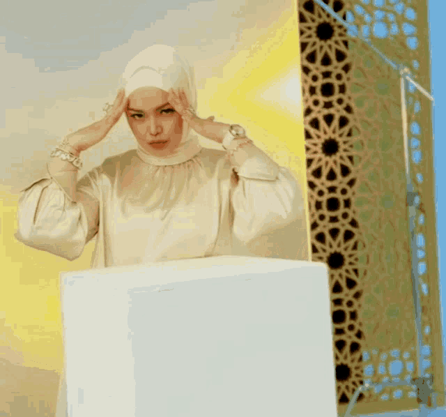 a woman in a white hijab holds her hands to her forehead