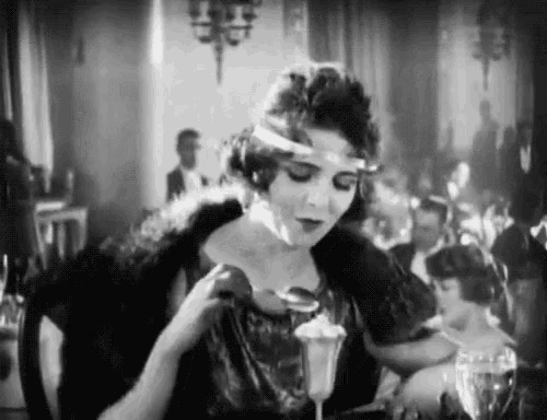 a woman is sitting at a table with a glass of wine and a spoon .