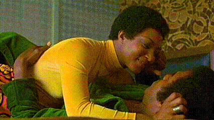 a man in a yellow shirt is laying on top of a man in a green blanket on a bed .