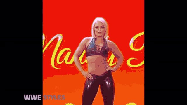 a woman in a black top and black pants is standing with her hands on her hips in front of a red background .