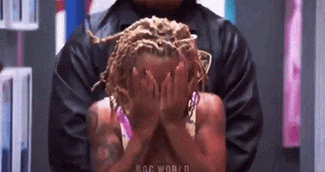 a woman with dreadlocks is covering her face with her hands in a room .