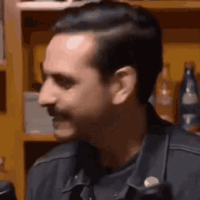 a man with a mustache is sitting in front of a shelf with bottles of beer .